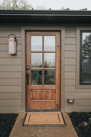 A wooden front door with a glass panel, a mailbox, and a small outdoor light fixture.