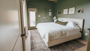 Un dormitorio con cama, lámpara colgante, puerta y ventana.