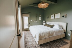 Un dormitorio con cama, lámpara colgante, puerta y ventana.