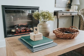 Una mesa de madera con un libro verde, un bloque de madera pequeño, un florero con flores y una cesta de mimbre.