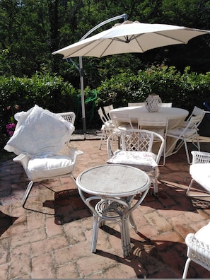 An outdoor patio with wicker furniture, including chairs and a table, under a large umbrella. - La Casa dei Ricordi in Buti (Buti)