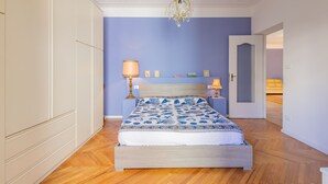 Un dormitorio con cama, candelabro, mesita de noche y una puerta que da a otra habitación.