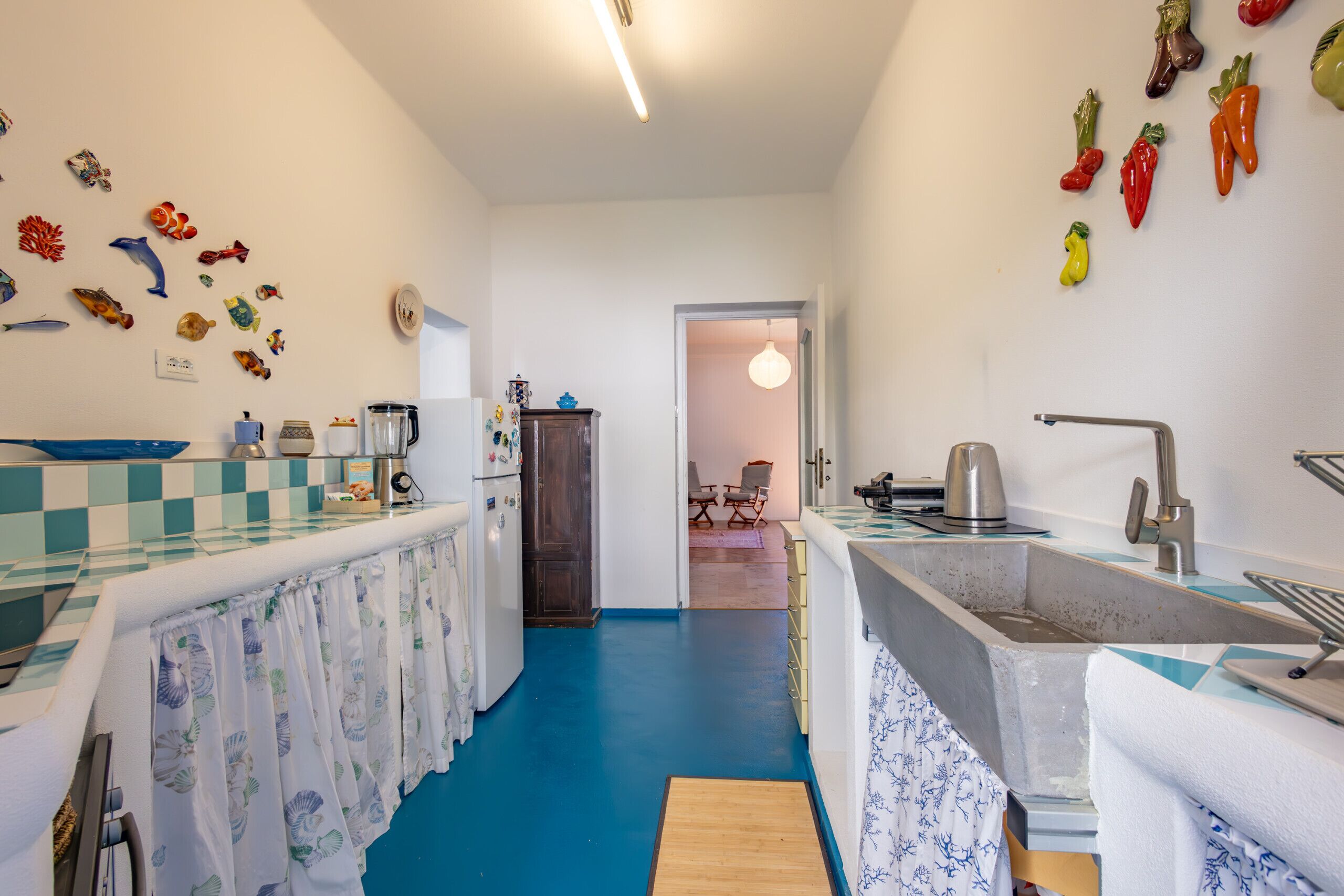 A kitchen with a blue floor, white walls, and a checkered backsplash. There are various kitchen appliances and a sink.
