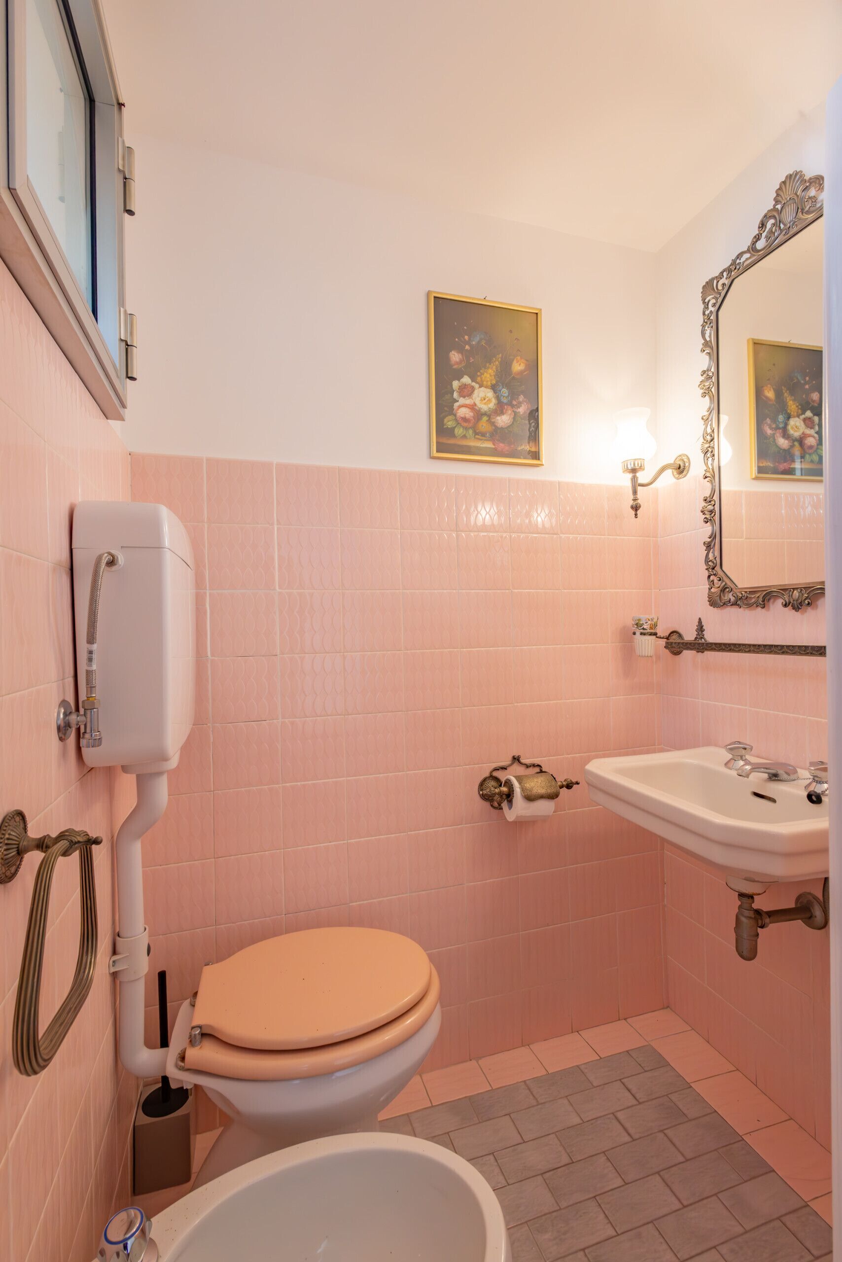 Ein Badezimmer mit rosa gefliesten Wänden, einer Toilette, einem Waschbecken und einer Badewanne.