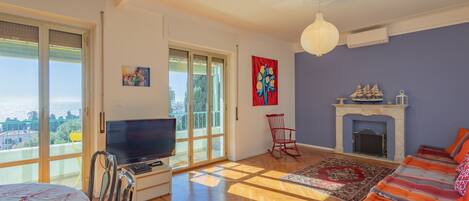 A spacious living room with a large window, a fireplace, a television, and a sofa.