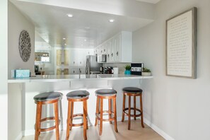 A modern kitchen with white cabinets, a central island with stools, and a framed inspirational quote on the wall.