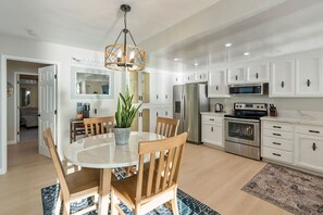A modern kitchen with white cabinets, stainless steel appliances, and a dining area with a round table and wooden chairs.
