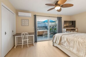 A bedroom with a bed, a desk with a chair, a ceiling fan, and a TV.