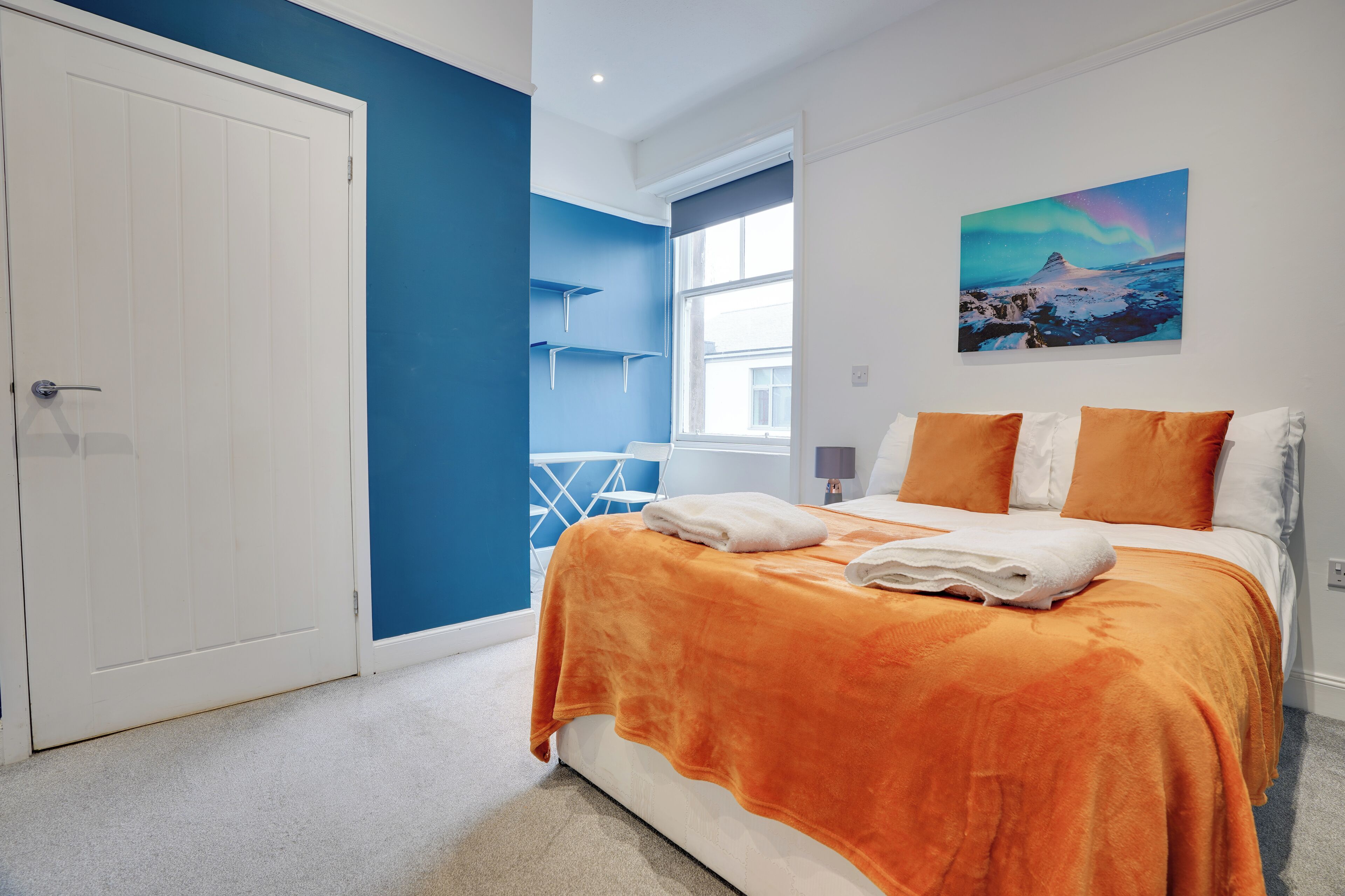 A bedroom with a bed, a window, a door, and a painting on the wall.