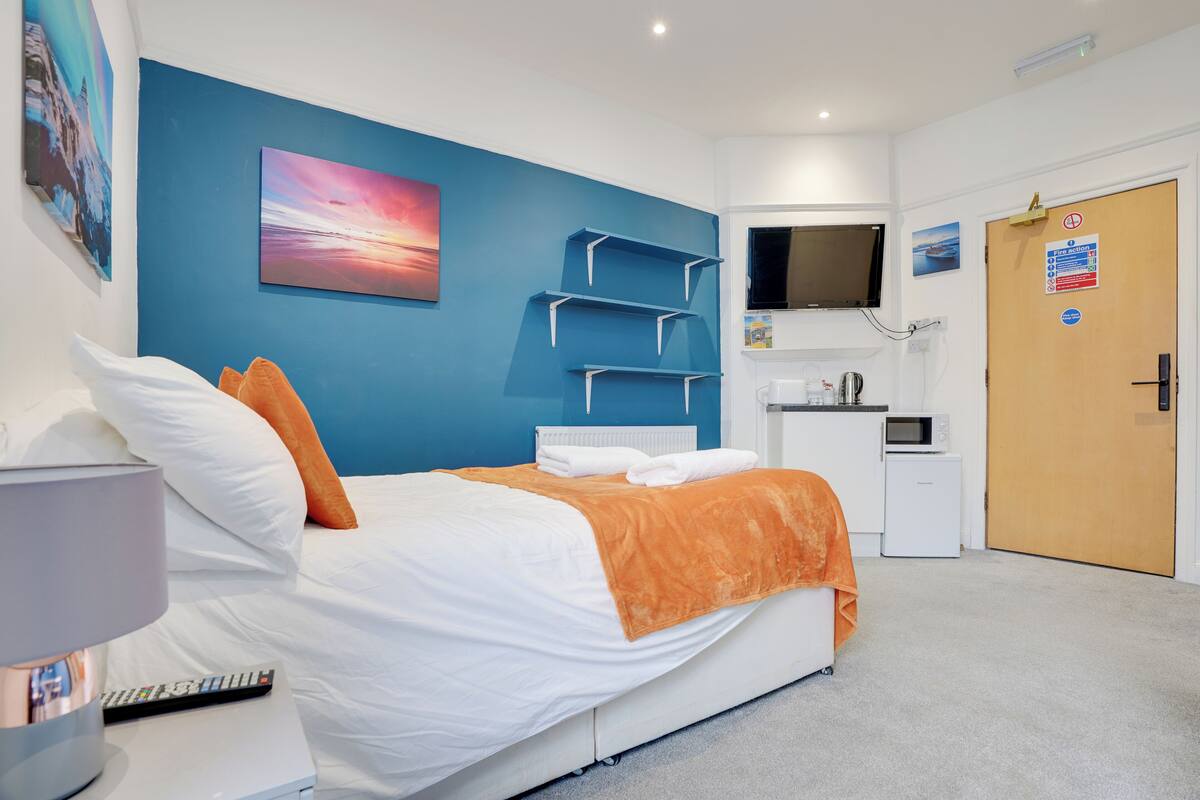 Una habitación de hotel con cama, televisor, escritorio con computadora y puerta con cartel.