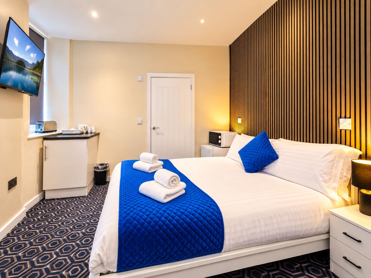 A hotel room with a bed, a television, a small kitchenette, and a wooden panel wall.
