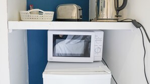 Une petite cuisine équipée d’un four à micro-ondes, d’un grille-pain, d’une bouilloire et d’un panier posé sur une étagère.