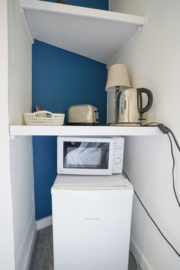 A compact kitchenette with a microwave, toaster, kettle, and a basket on a shelf. - Homesly Guest Rooms - Self Checkin (Berwick-upon-Tweed)