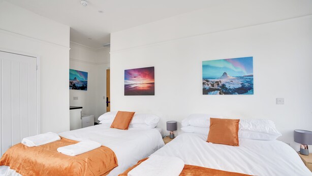 Une chambre d’hôtel avec deux lits, du linge de lit blanc, des plaids orange et deux tableaux au mur.