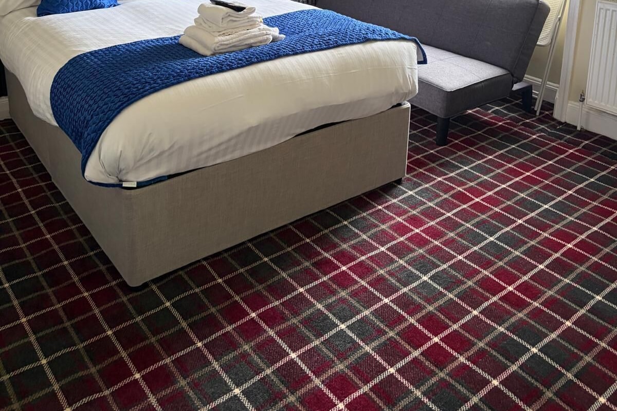 A hotel room with a bed, a sofa, a window with a view, and a plaid-patterned floor.