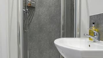 Un baño moderno con ducha envuelta en vidrio, un lavabo blanco y un revestimiento de mármol en la pared de la ducha.