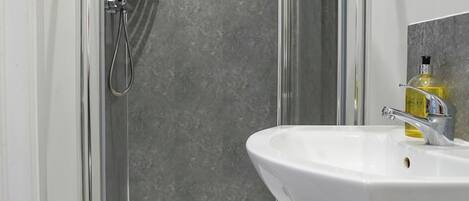 A modern bathroom with a glass-enclosed shower, a white sink, and a marble-tiled shower wall.