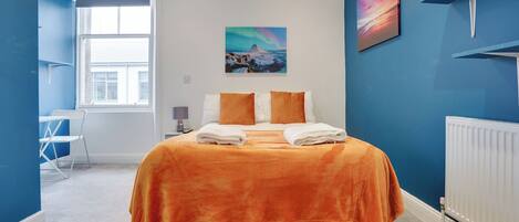 A bedroom with a bed, a window, a painting, and a radiator.