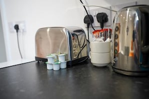 A kitchen counter with a toaster, a coffee maker, and several coffee pods. - Homesly Guest Rooms - Self Checkin (Berwick-upon-Tweed)