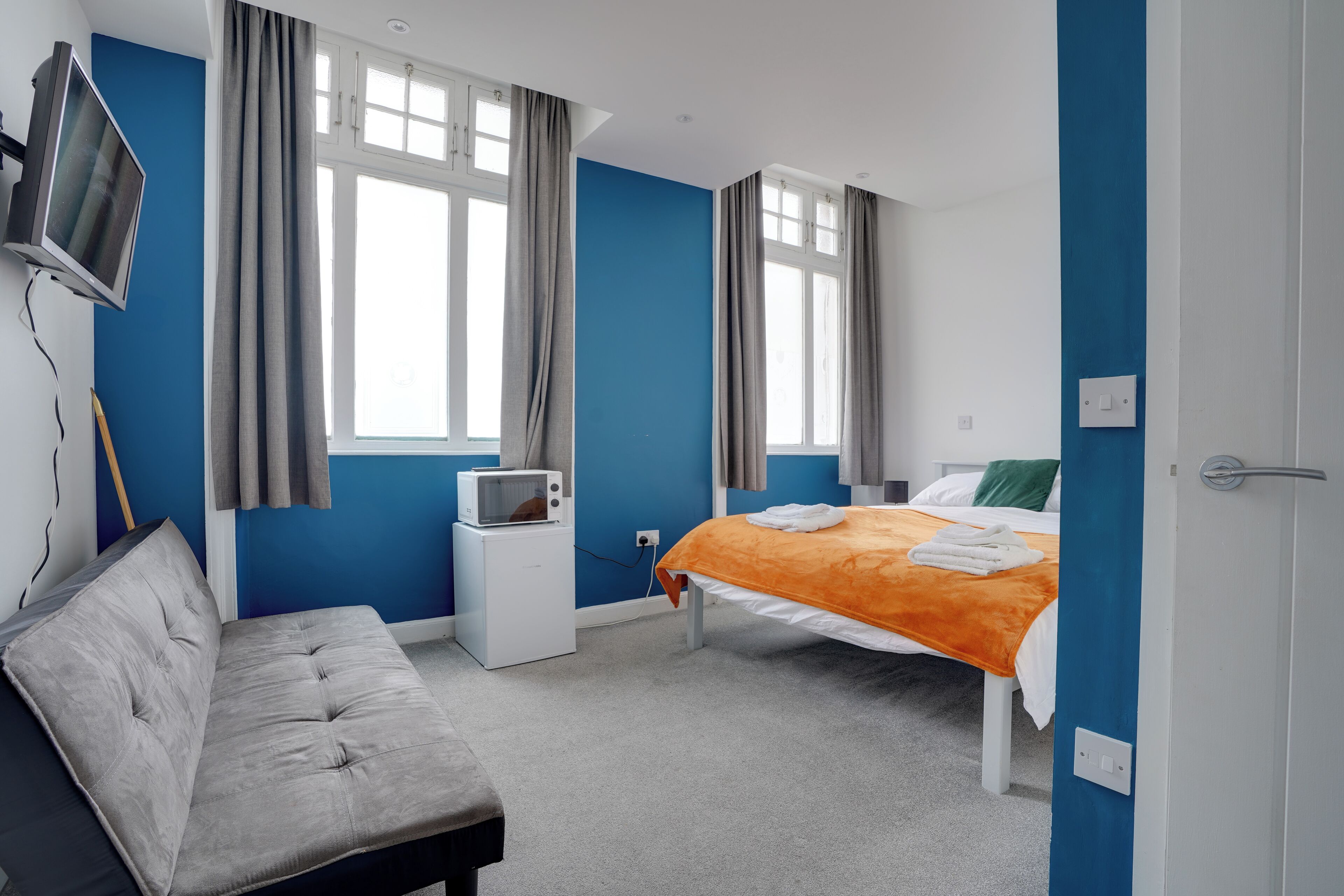A bedroom with a bed, a TV, a microwave, and a couch.