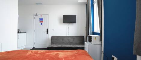 Een hotelkamer met een bed, een aan de muur bevestigde televisie, een klein bureau en een raam met gordijnen.