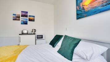 Una cama bien hecha con almohadas blancas y verdes, una colcha amarilla y una pared con cuatro cuadros enmarcados.