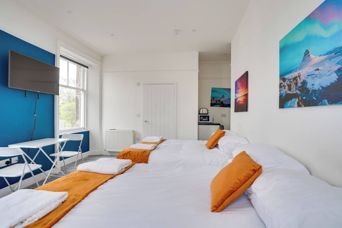 Habitación de hotel con una cama grande, un escritorio, sillas, una puerta blanca y un cuadro en la pared.