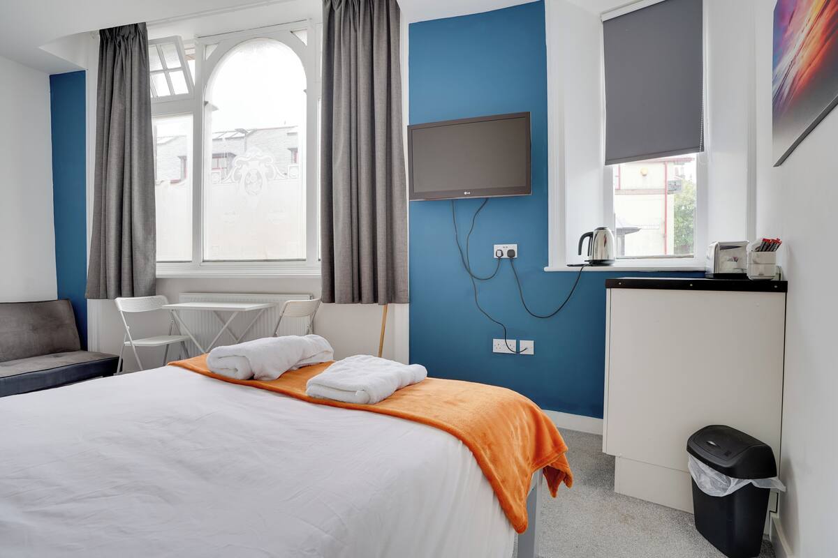 Habitación de hotel con cama, escritorio, silla, televisión y ventana con cortinas.