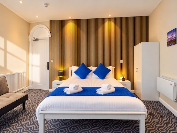 Una habitación de hotel con una cama grande, dos mesitas de noche, un armario y una alfombra estampada.