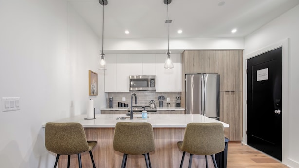 A modern kitchen with a central island, bar stools, stainless steel appliances, and pendant lighting. - Capitol Hill Suites - Unit 9 (Washington)
