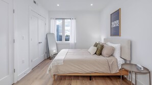 A modern bedroom with a bed, a bedside table, a chair, a window with curtains, and a framed picture on the wall. - Capitol Hill Suites - Unit 9 (Washington)