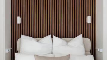 Ein Bett mit weißer und beiger Bettwäsche, eine Wand aus Holzleisten und zwei an der Wand befestigte Leuchten.