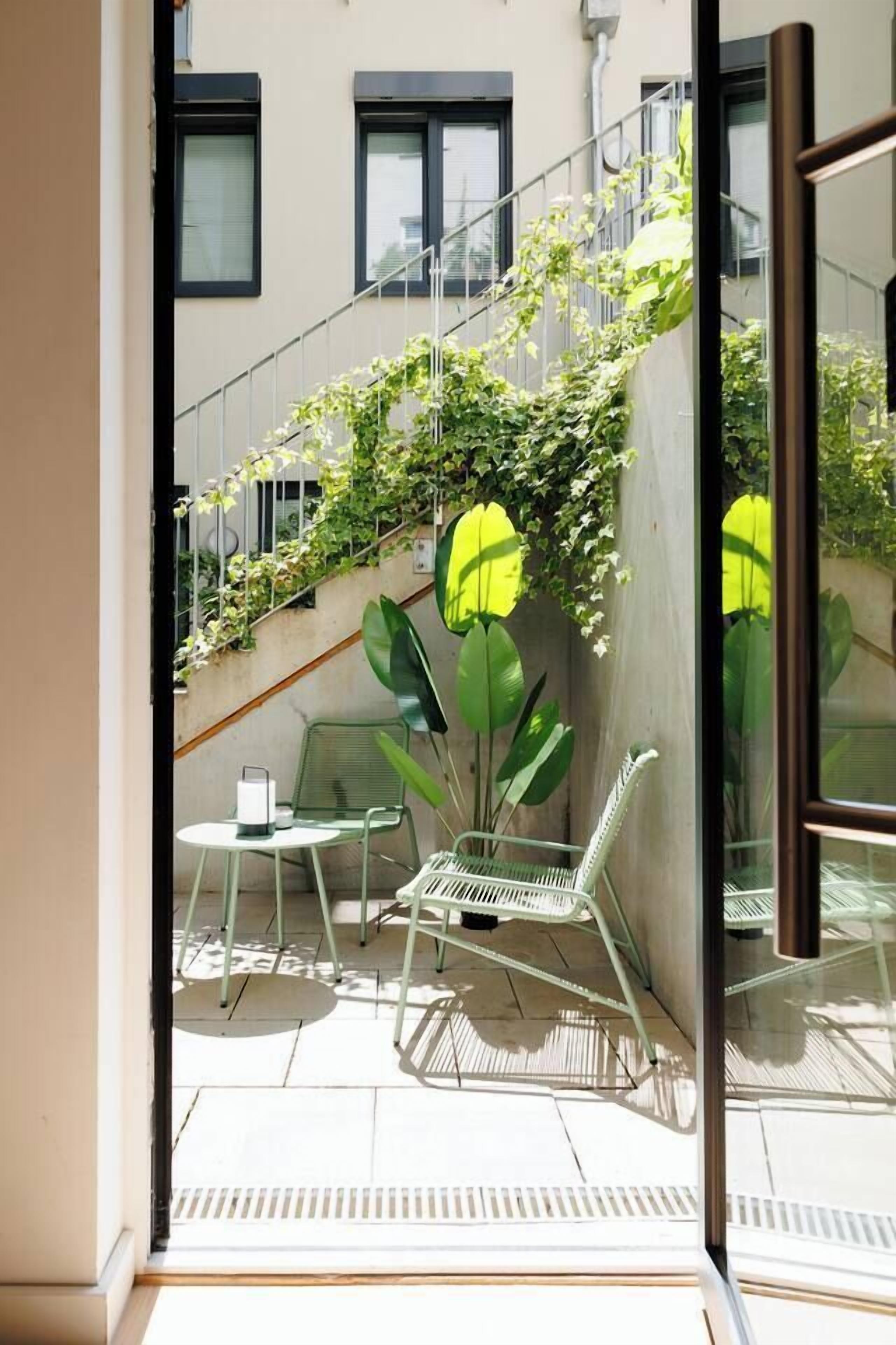 Ein Balkon mit Tisch und Stühlen, eine Treppe mit Bepflanzung und ein Fenster mit Blick auf Gebäude.