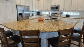 Een moderne keuken met witte kastjes, granieten aanrechtbladen, roestvrijstalen apparatuur en een centraal eiland met barstoelen.