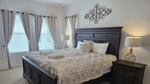 Een slaapkamer met een donker houten bed, beddengoed met een beige patroon, twee bedlampjes en een decoratief wandobject.