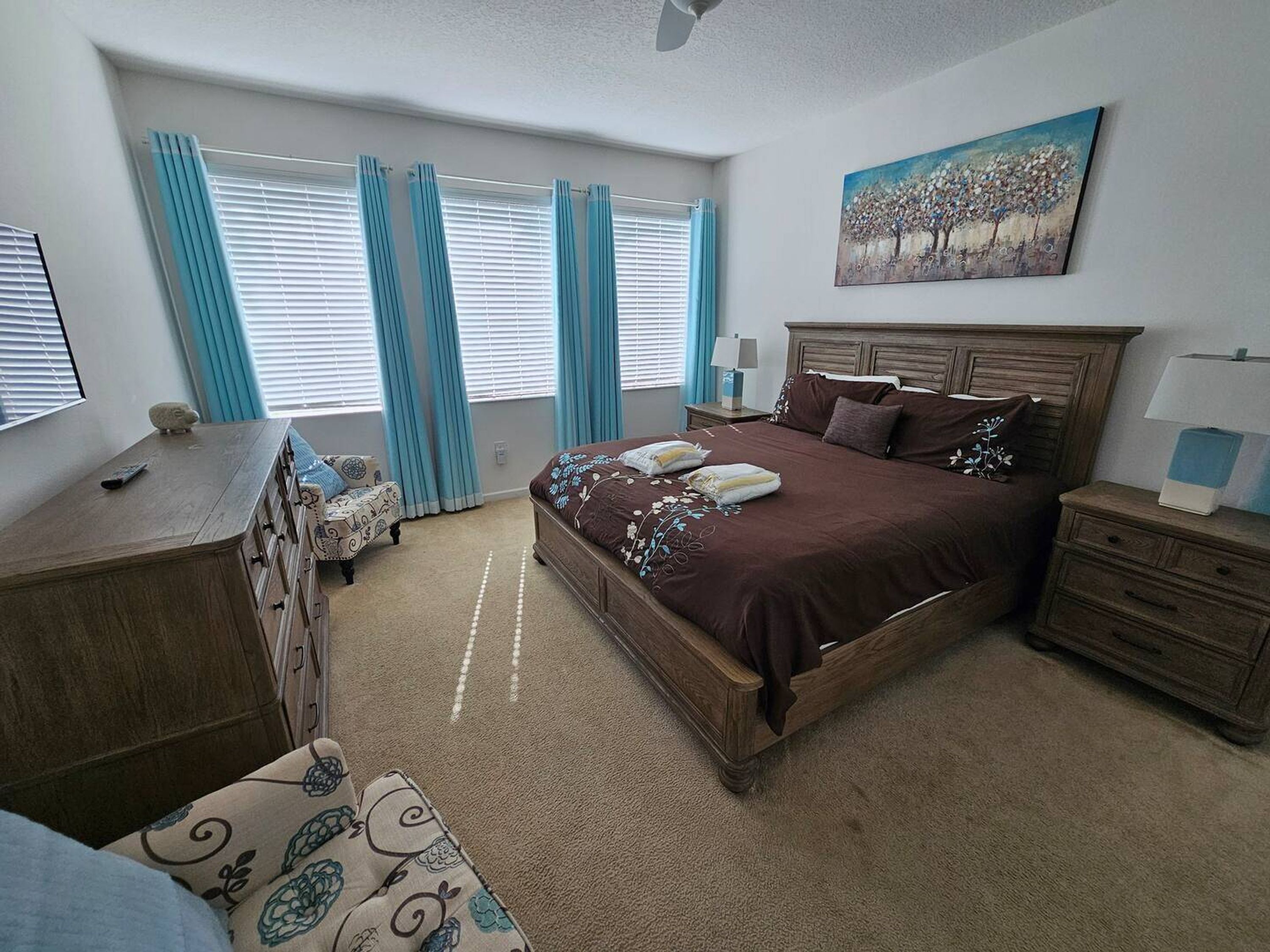 Une chambre à coucher avec un grand lit, une commode, une chaise et un tableau accroché au mur.