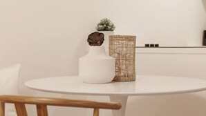 A round white table with a woven basket and a white vase with a plant.