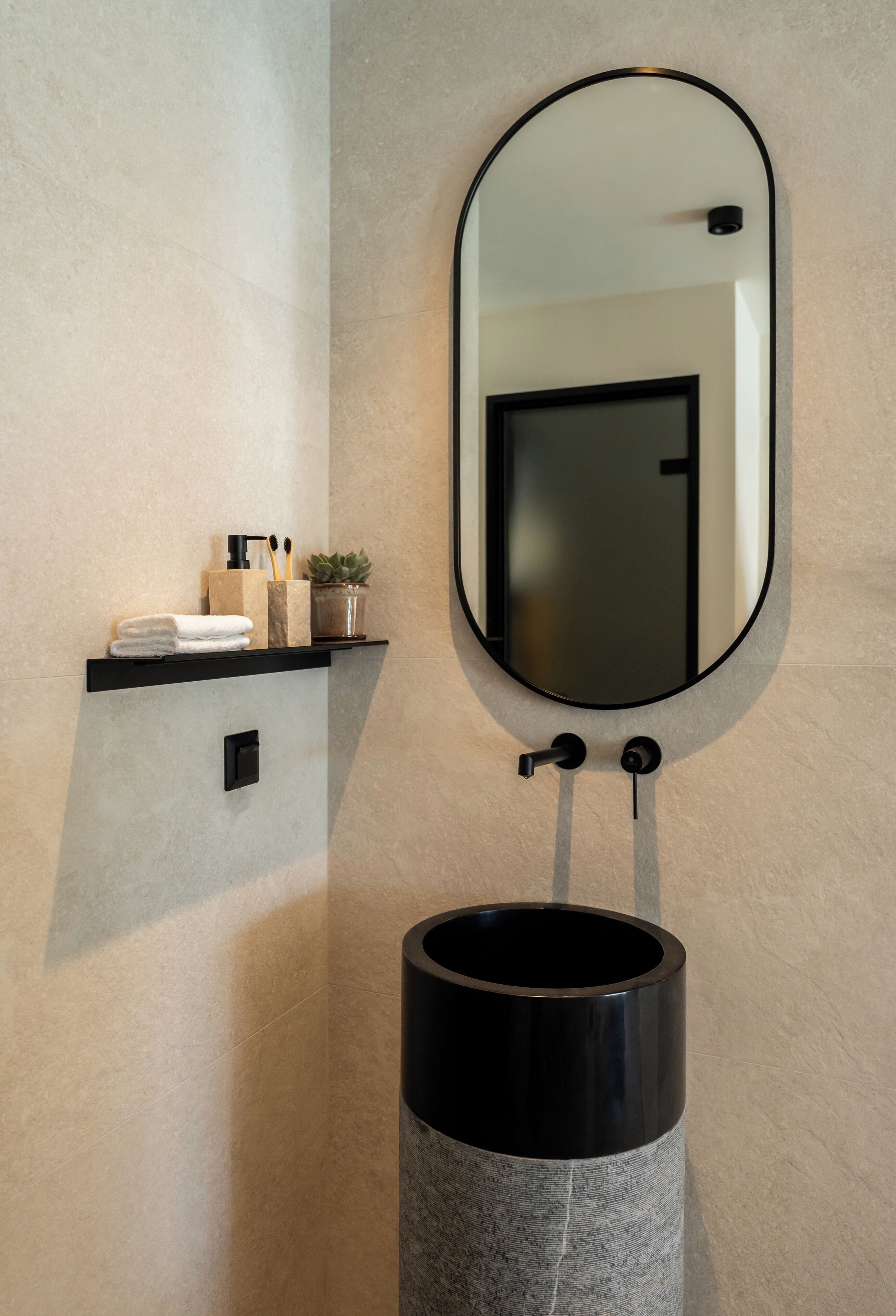A bathroom with a round sink, a mirror, and a shelf with toiletries.