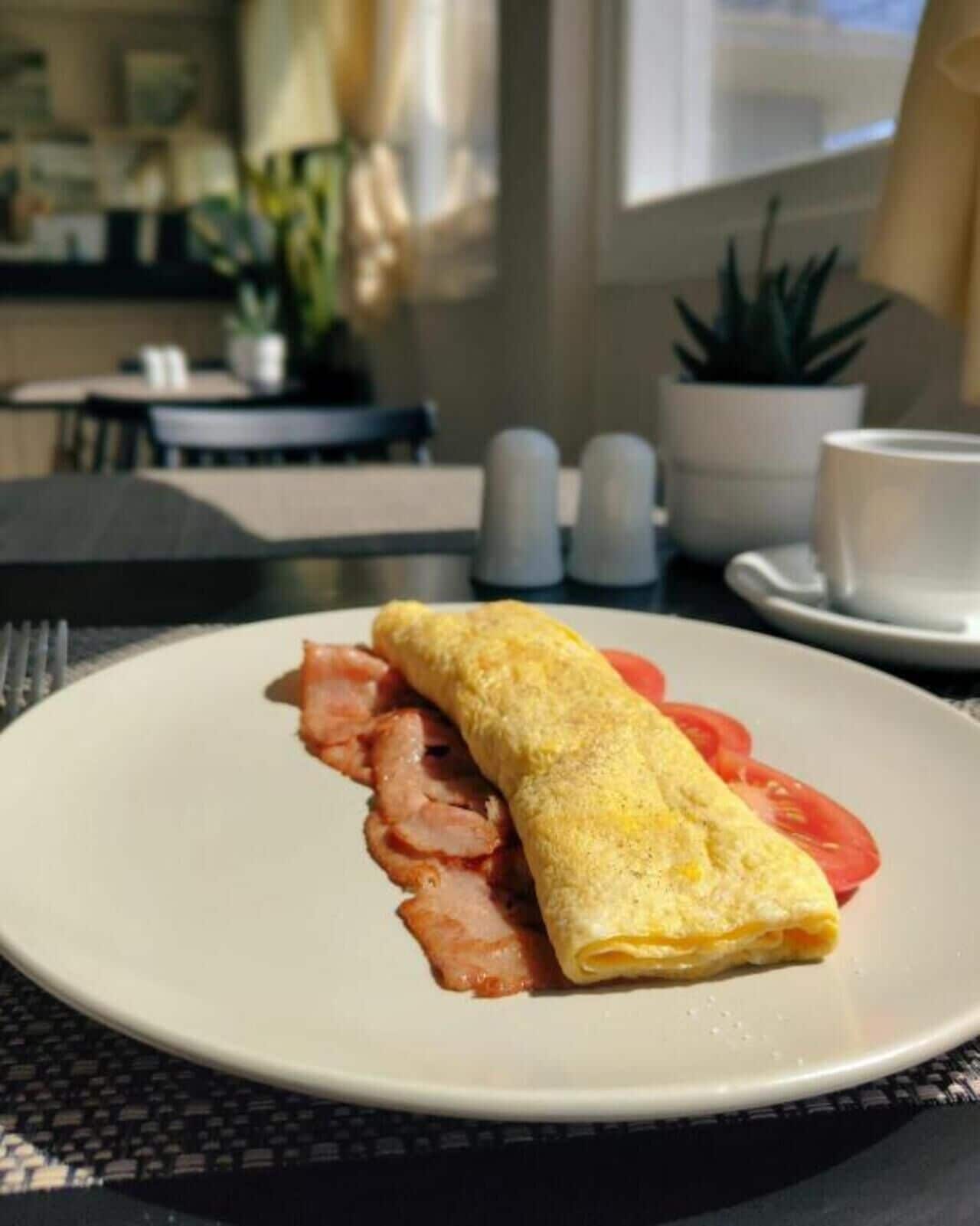 A plate with a rolled omelette, bacon, and tomato slices on a table in a dining area.
