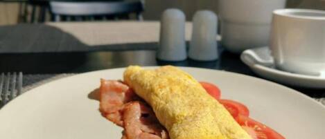 A plate with a rolled omelette, bacon, and tomato slices on a table in a dining area.