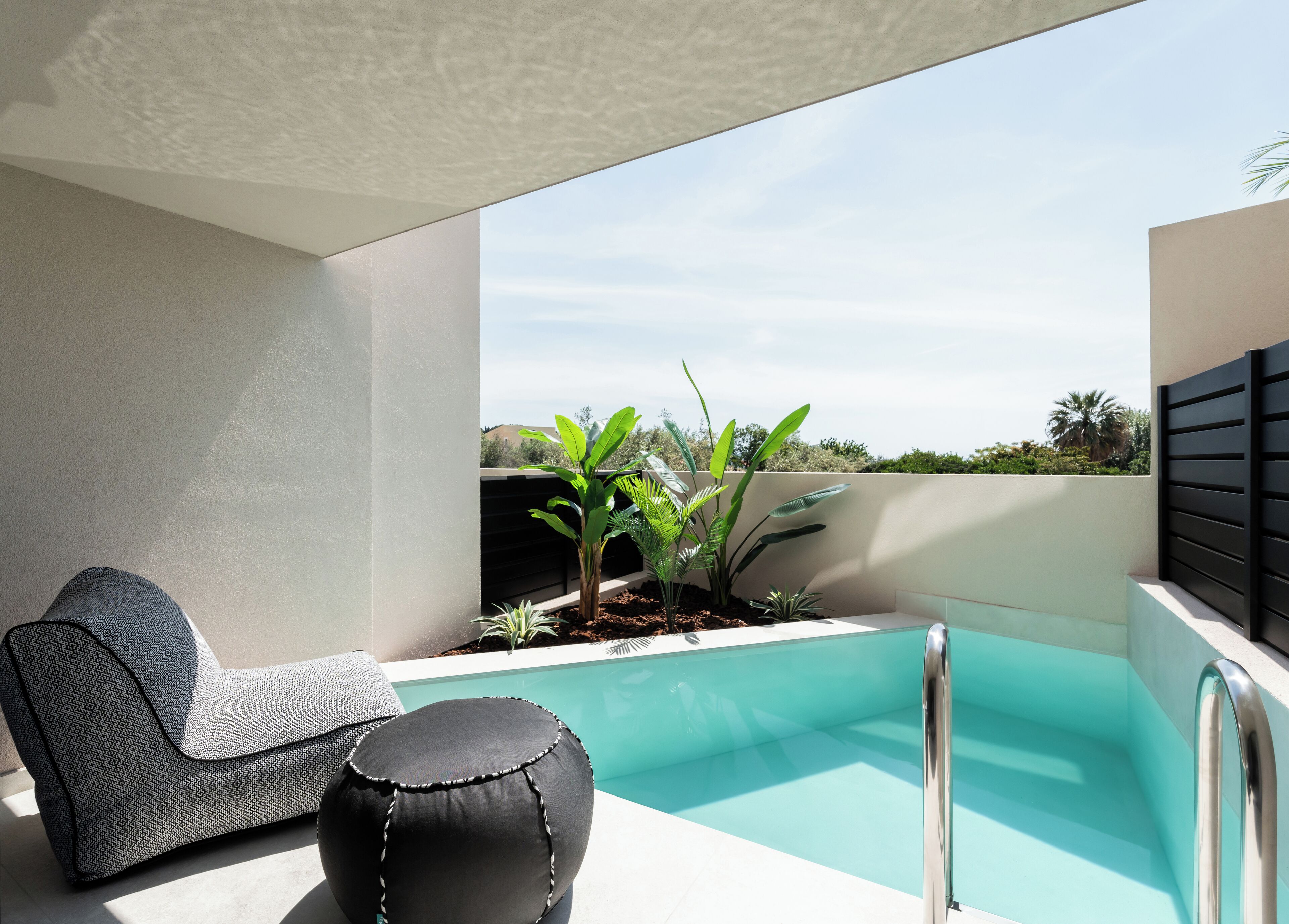 A modern outdoor pool area with a lounge chair and ottoman, surrounded by greenery and a clear view of the landscape.