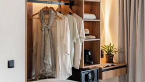 Um closet espaçoso com prateleiras de madeira, um cabideiro com roupas, um vaso de planta e uma pequena mesa com um livro e um abajur.