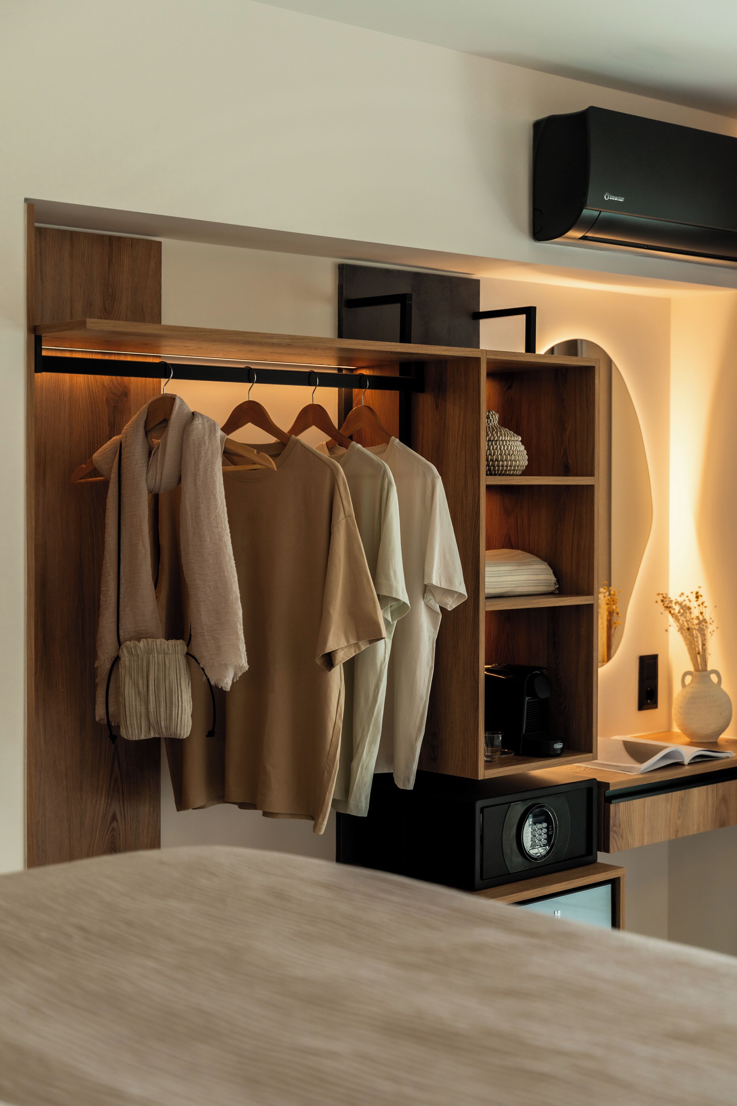 Un dormitorio con cama, un armario con ropa colgada, una mesita de noche con lámpara y un aire acondicionado instalado en la pared.