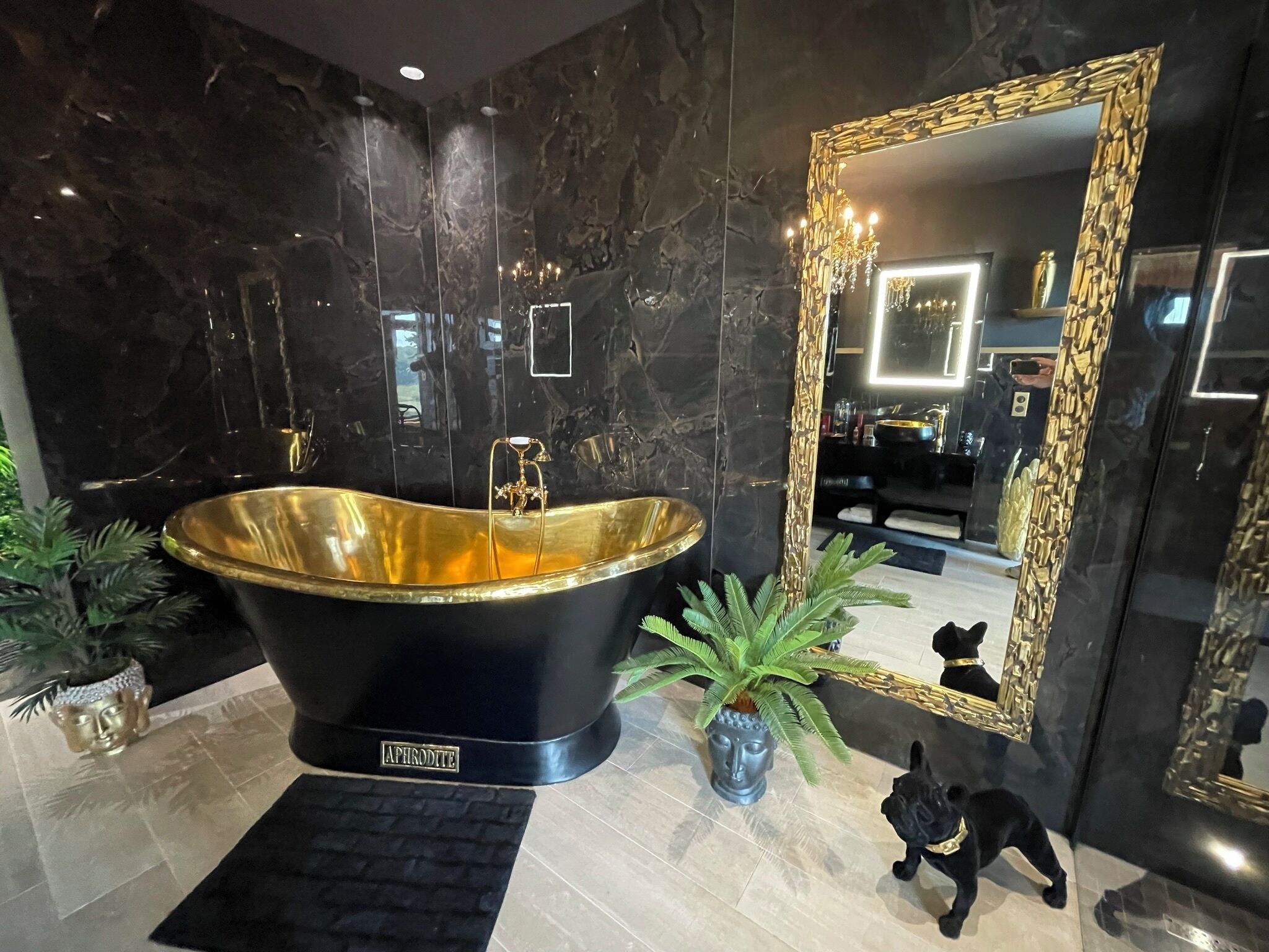 A modern bathroom with a freestanding bathtub, a large mirror with a gold frame, and a Buddha statue.