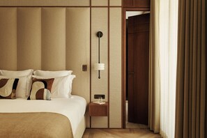 Quarto de hotel com uma cama grande, mesa de cabeceira com luminária e vista para o corredor.