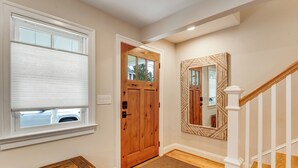 Un pasillo con una puerta de madera, un banco, un espejo y una escalera.