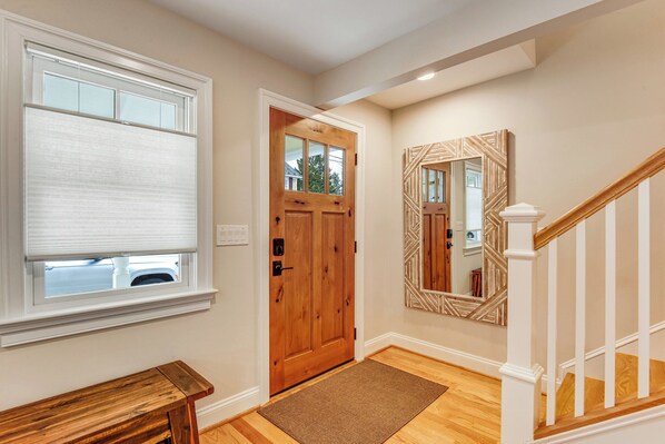 A hallway with a wooden door, a bench, a mirror, and a staircase.