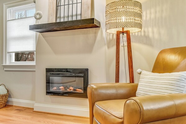 A living room with a fireplace, a brown leather sofa, a floor lamp, and a window with blinds.
