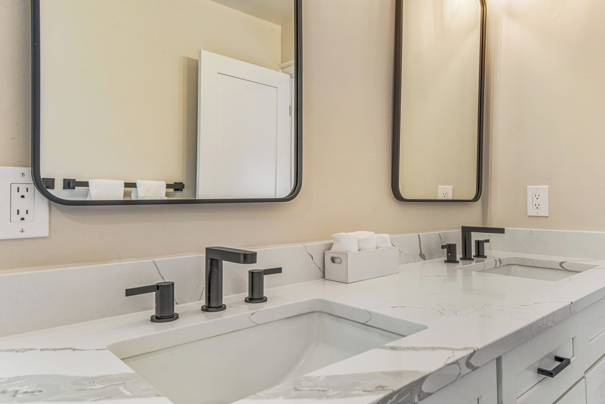A bathroom with two sinks, a mirror, and a towel dispenser.