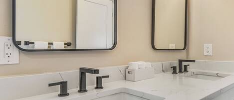 A bathroom with two sinks, a mirror, and a towel dispenser.